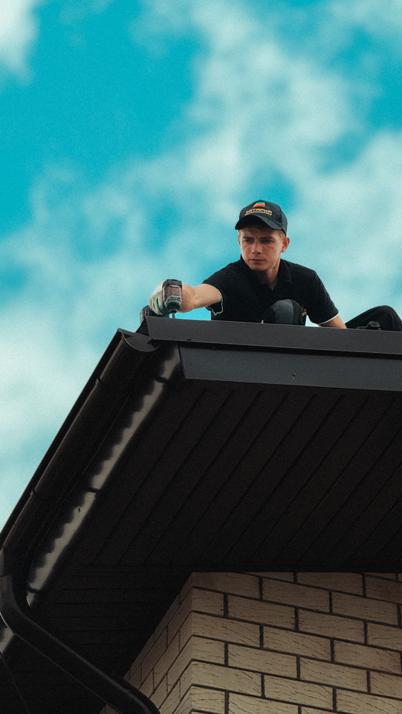 Gutter installer working along a roofline under a blue sky