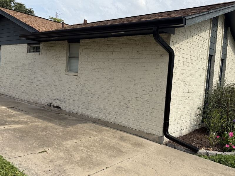 Black seamless gutter and full downspout run on white brick in Portland by J Seamless Gutters